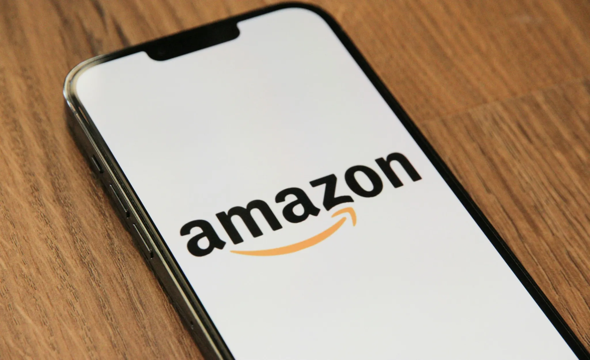 Smartphone displaying the Amazon logo on a wooden surface, highlighting e-commerce and tech branding.