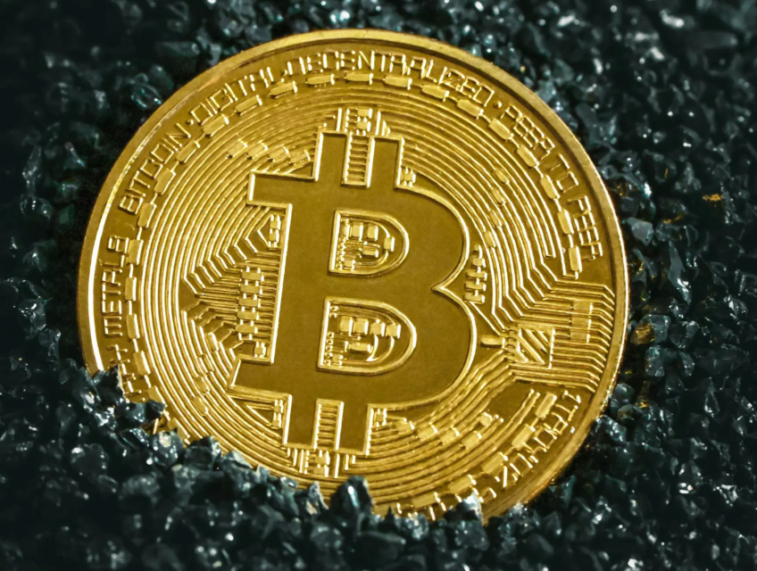 A close-up of a golden Bitcoin coin placed on a bed of dark, glistening stones, symbolizing the value and prominence of cryptocurrency in modern finance.