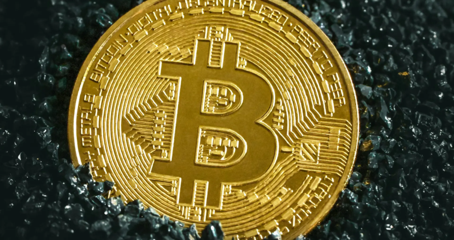 A close-up of a golden Bitcoin coin placed on a bed of dark, glistening stones, symbolizing the value and prominence of cryptocurrency in modern finance.