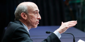Gary Gensler, président de la SEC, prenant la parole lors d'un événement public, faisant un geste de la main tout en étant assis devant un microphone