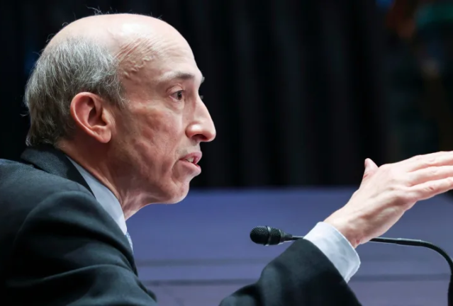 Gary Gensler, président de la SEC, prenant la parole lors d'un événement public, faisant un geste de la main tout en étant assis devant un microphone